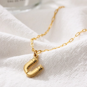 Close-up of golden stainless steel U-shaped initial pendant with bubble texture finish