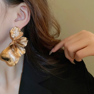 Detailed close-up of oversized gold floral earrings with a brushed metallic texture