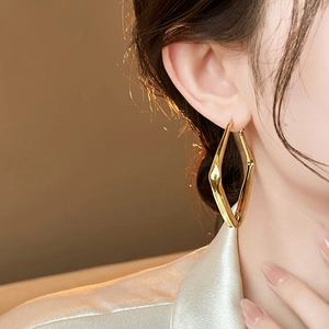 Close-up of golden geometric earrings on model showing glossy finish and twisted style