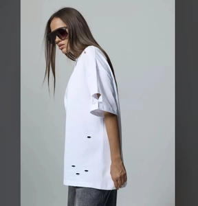 Close-up of distressed white oversized t-shirt featuring artistic ripped hole details