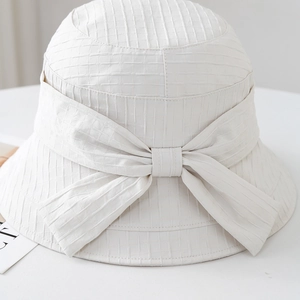 Dettaglio di un cappello a secchiello bianco con trama a griglia 3D e un grande fiocco