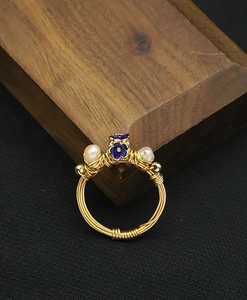 Macro detail of handmade wire-wrapped ring with blue enamel flower and baroque pearls