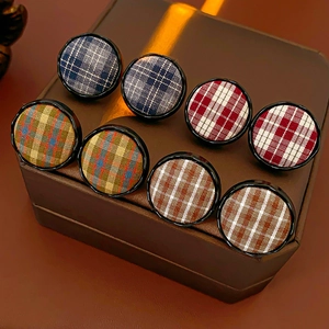 Macro shot of circular tartan fabric earrings in various colors on leather display stand