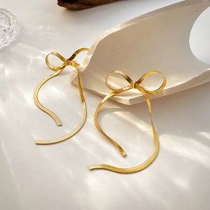 Detail of 18K gold bow earrings with elegant long snake chain tassels on white background