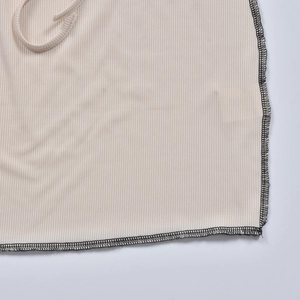 Détail du tissu en maille côtelée beige avec couture surjetée noire précise