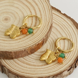 Détail de créoles en acier doré 18 carats avec breloques papillon et perles naturelles