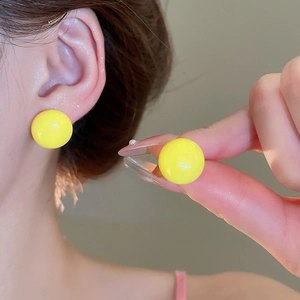 Close-up of vibrant yellow spherical stud earrings with a glossy polished finish