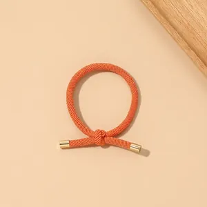 Detail of high-elastic orange braided hair tie with elegant gold metal end caps