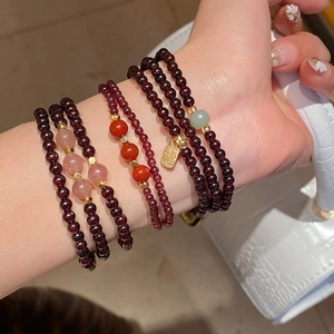 Detail of layered garnet and strawberry quartz bracelets with a gold Fu charm on wrist