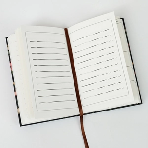 Detail of open notebook showing dotted lined pages, brown silk ribbon, and floral back cover