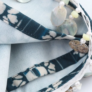 Macro shot of light blue tie-dye fabric with handmade beads and shell pendants