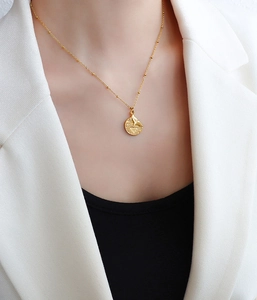 Close-up of 18k gold fishtail and wave round pendant on a fine bead chain necklace