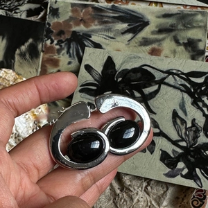 Macro shot of silver retro brooch featuring oval black stones against artistic cards