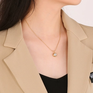 Detail of a minimalist gold necklace with a round sparkling zircon pendant on a snake chain