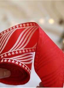 Close-up of red Christmas ribbon with white feather pattern and stitched edges for gifts