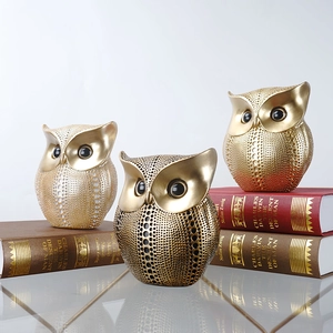 Three golden resin owl figurines with cutout patterns displayed on vintage books