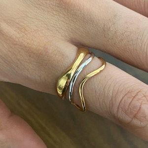 Three-piece 18K gold and silver wavy layered open rings worn on person's hand