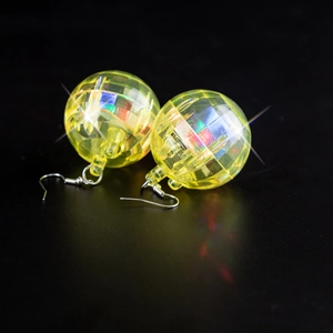 Macro shot of yellow faceted disco ball earrings reflecting light on a dark surface