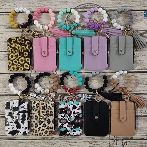 Multiple silicone bead bracelets with leather card holders and tassels on wood background
