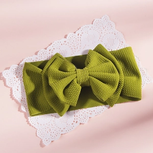 Macro detail of grass green waffle knit baby headband featuring a large bow on pink background