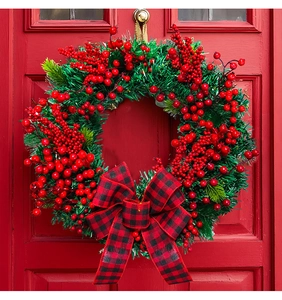Close-up of a Christmas wreath with red berries and plaid bow on a red door background