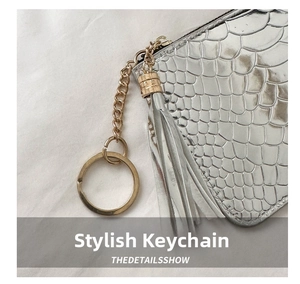 Detail of silver crocodile-embossed clutch with metallic tassel charm and polished hardware