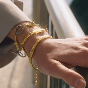 Outdoor shot of layered hammered gold bangle and lava-style chain bracelets on wrist