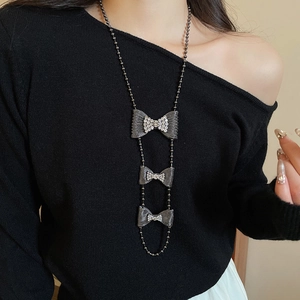 Close-up of sparkling bow pendant tassel necklace on dark knitwear showing metallic texture