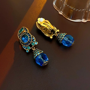 Detail of vintage gold earrings with blue crystals and green gems on a clip-on back