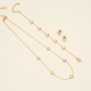 Flat lay of gold necklace, bracelet, and earrings set with white pearls on beige background