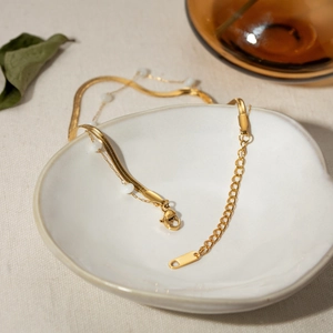 Double-layer 18K gold stainless steel snake chain with shell beads in a white ceramic dish