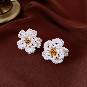Detailed view of handmade white camellia pearl earrings with gold bead centers on silk