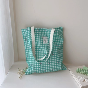 Detail of green and white checkered cotton tote bag with floral print and woven straps