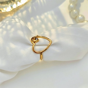 Detailed view of a gold open heart ring with a small diamond on white silk fabric