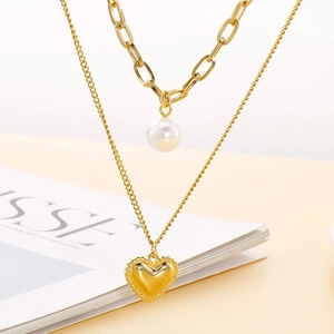Collier double rang doré avec perle baroque et pendentif cœur sur fond beige