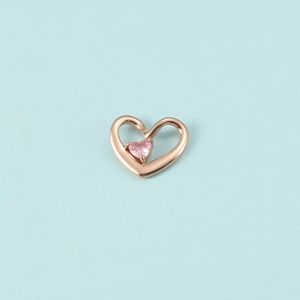 Gros plan du pendentif cœur en or rose avec pierre de naissance rose sur fond bleu