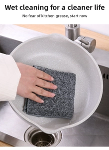 Thick charcoal fiber cloth cleaning grease from a metal pot in a kitchen sink