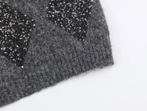 Detailed close-up of grey knitted vest with sparkling black and silver sequined heart patch