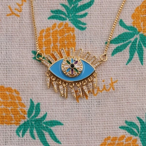 Detailed close-up of a gold-plated Evil Eye pendant necklace with blue enamel on fabric