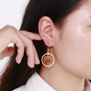 Detailed view of gold angel wing drop earrings worn on ear with round frame and crystal