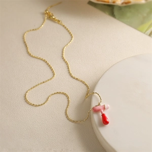 Vue détaillée du collier doré avec pendentif abstrait en émail rose et rouge sur socle