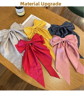 Detail of five oversized satin bow hair clips in multiple colors on a wooden table