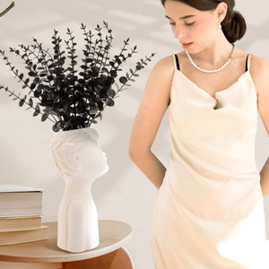 Artificial black eucalyptus leaves in a human face ceramic vase for minimalist home decor