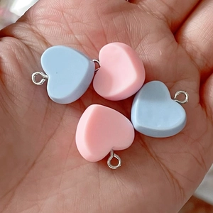 Handheld view of pink and blue resin heart charms with metal loops for DIY jewelry making