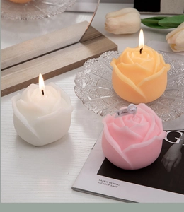 Detailed view of burning rose-shaped scented candles in white, yellow, and pink colors
