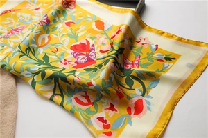 Detail van gele zijden sjaal met bloemen, vlinders en een elegante satijnen textuur
