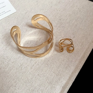 Elegant gold hollow geometric bangle and ring jewelry set on a minimalist textured fabric