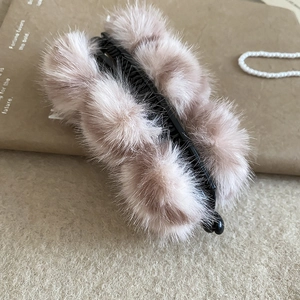 Détail d'une pince banane avec pompons en peluche rose clair sur fond chaud texturé