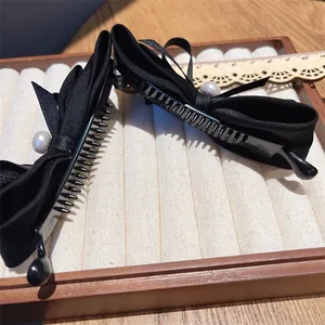 Close-up of black ribbon bow hair clips with white pearls on a wooden display tray