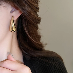 Gros plan d'élégantes boucles d'oreilles goutte d'or en forme de C portées par un mannequin